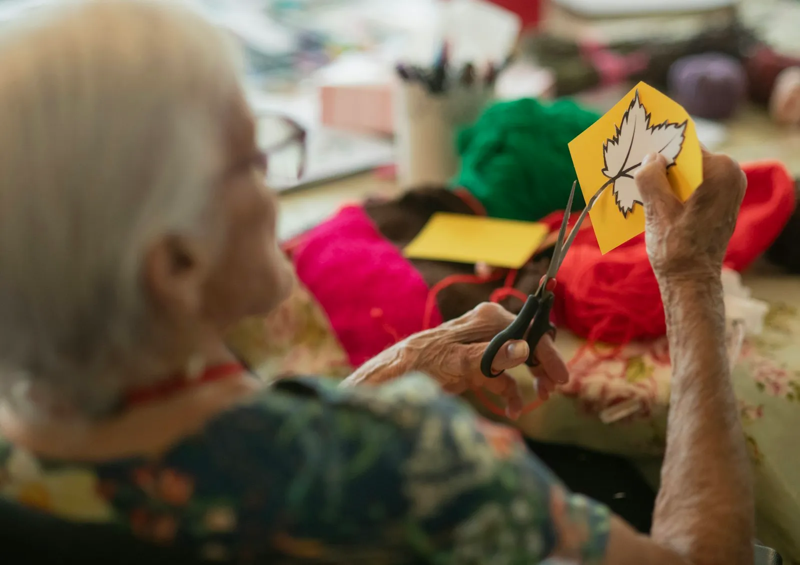 An older woman cutting out a paper autumn leaf