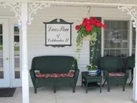 The front porch of Drews Place of Coldwater II, with wicker chairs and a hanging basket of red flowers