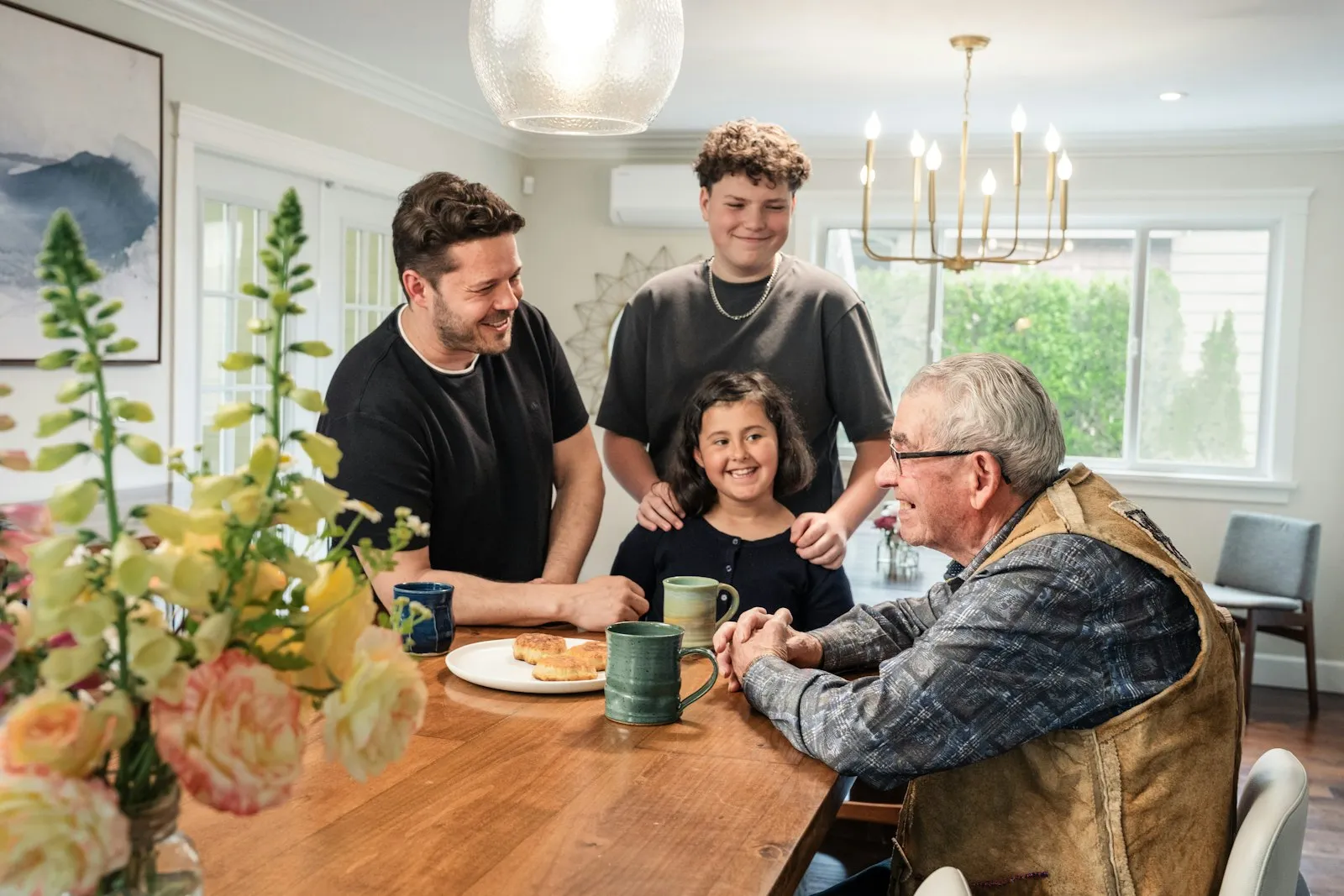 A grandfather laughing with his family over coffee at a dining table