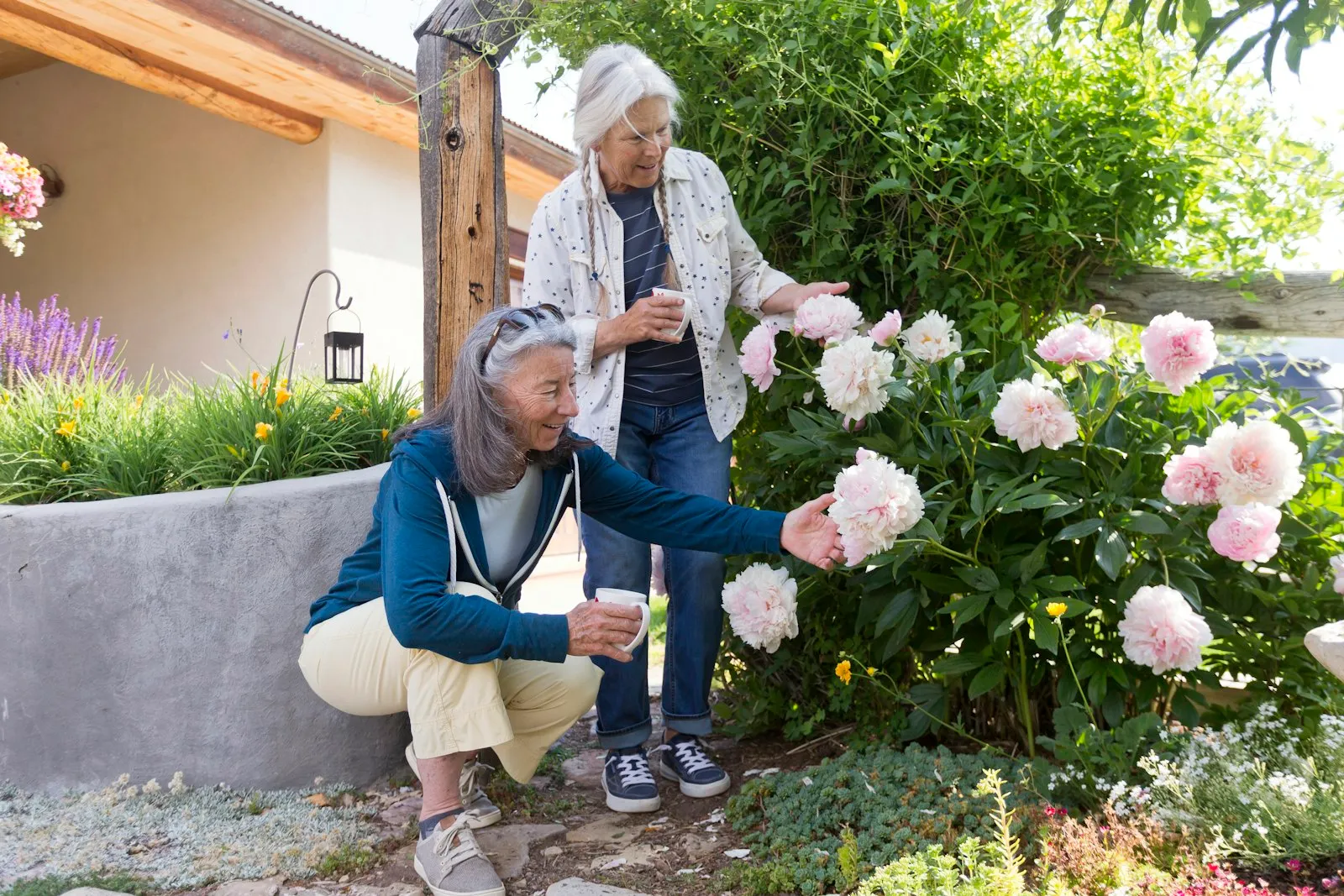 Two women admiring pink peonies in a garden