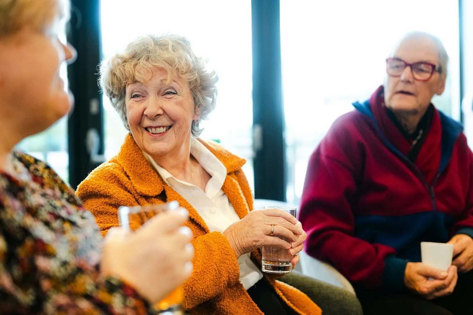 A smiling older woman in an orange coat chatting with friends