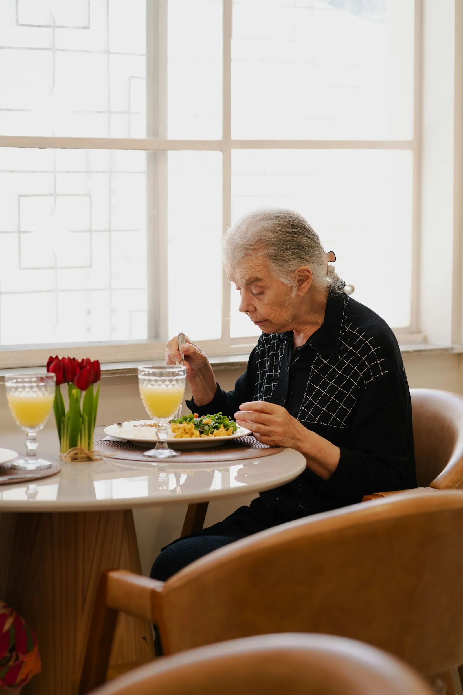 An older woman enjoying a meal at a table by a sunny window