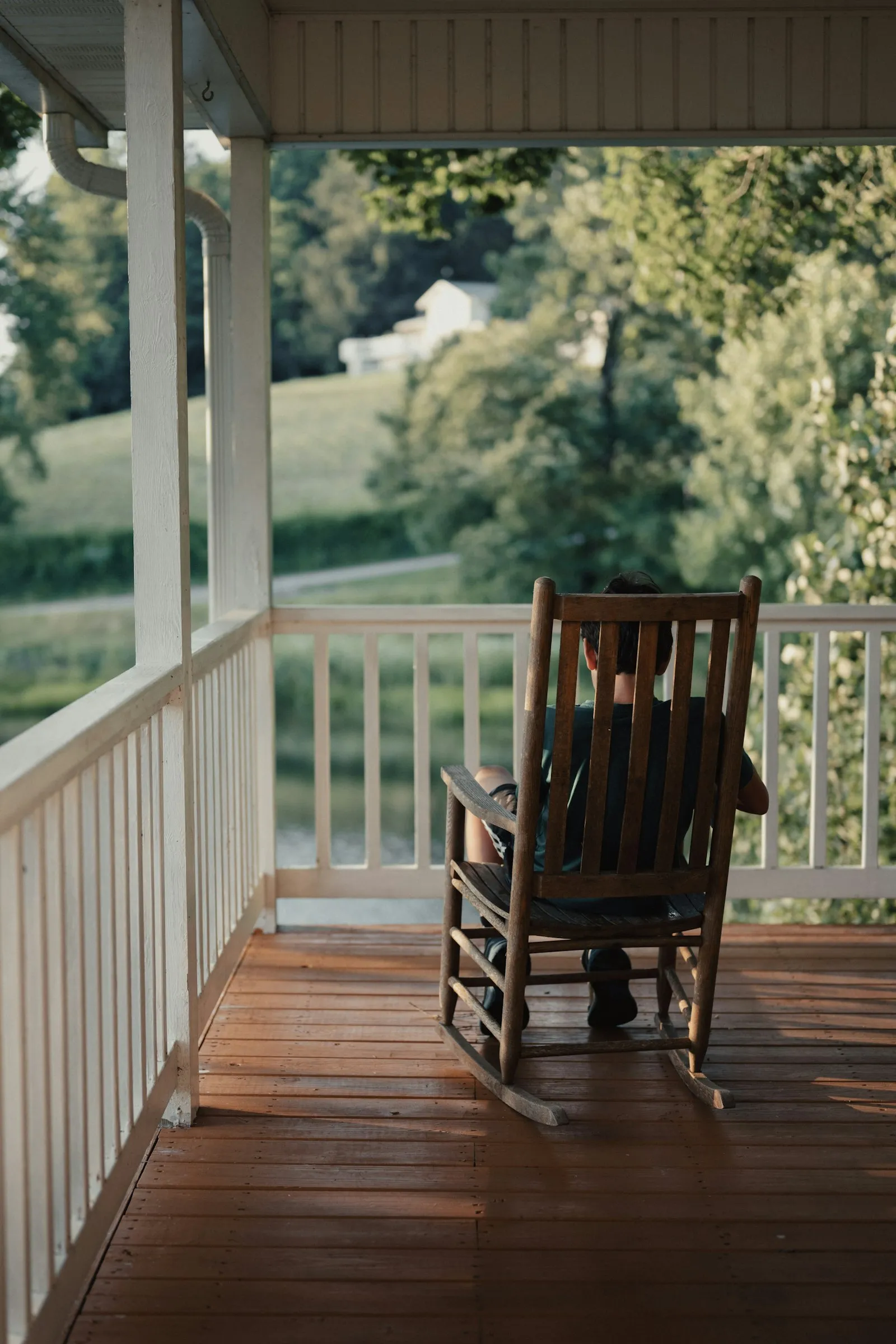 A wooden rocking chair on a quiet porch overlooking green trees